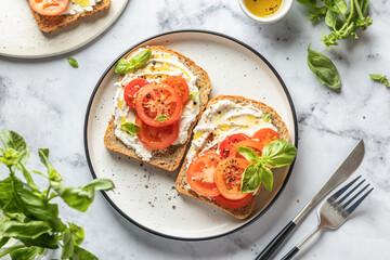 Sandwiches with tomatoes, cream cheese, olive oil and basil on a plate on white marble background....