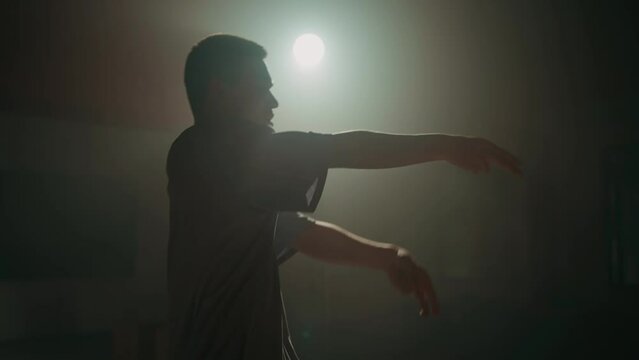 Young man dancing contemporary hip hop on red background with white light in studio wearing white shirt. Shooting of modern slow dance choreography. Motion of male dancer expressing feelings in dance