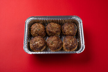 Juicy Fresh Beef Meat Patties in Disposable Foil Packaging on a Red Background.
