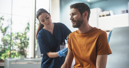 Happy Caucasian Man Sitting In The Chair In Bright Hospital And Getting His Hepatitis B Vaccine. Professional Female Nurse Is Performing Injection And Putting A Patch On. Public Healthcare Concept. - obrazy, fototapety, plakaty