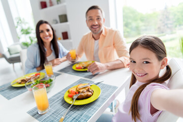 Portrait of cute small girl make selfie peaceful parents eat domestic food drink juice morning apartment indoors