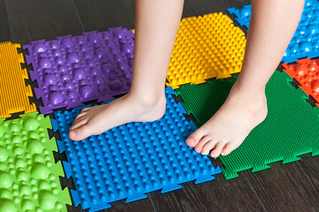 The child is engaged in orthopedic massage mats for legs of different hardness and texture. Massage of the nerve endings of the legs, prevention of flat feet in children. Treatment of foot deformity - obrazy, fototapety, plakaty
