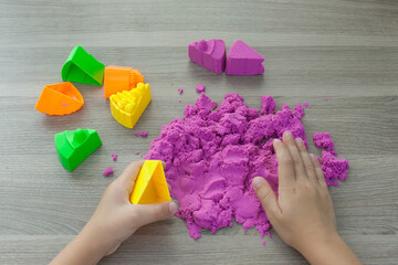 Little girl playing with bright kinetic sand at table indoors, closeup