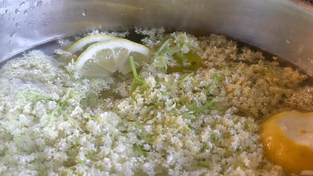 Elderberry flowers, slices of cut lemon in hot water, adding two tablespoons of vinegar and mixing with wooden spoon and covering pot with lid - preparation of healthy, natural homemade drink.