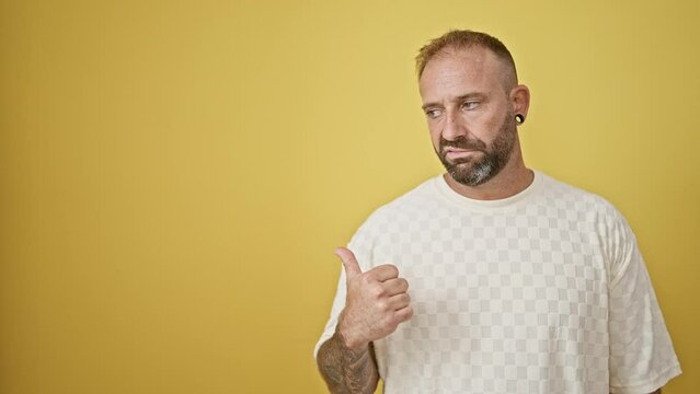 Young man pointing to the side saying no with head over isolated yellow background