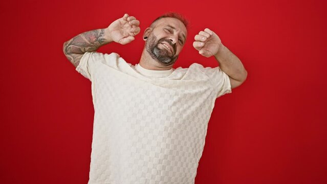 Exhausted young man caught on camera, stretching back and yawning over an isolated, red background