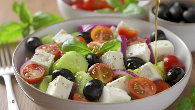 Pouring olive oil into a bowl of traditional Greek salad. Fresh vegetable salad with feta cheese.