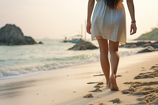 Closeup of female bare feet in long skirt walking on the sandy sea beach at sunset