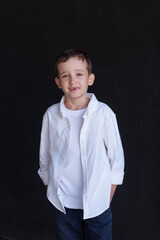 Portrait of a 6-year-old boy in a white shirt against a black wall. Smiles widely, one front tooth is missing, fell out. 