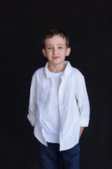 Portrait of a 6-year-old boy in a white shirt against a black wall. Smiles widely, one front tooth is missing, fell out. Banner