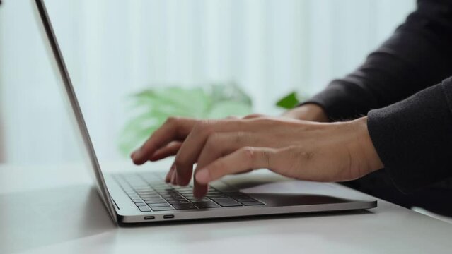 The man's hand is typing on a laptop computer keyboard at home or in the office. He is working, sending messages, chatting, browsing the internet, and using social networking.