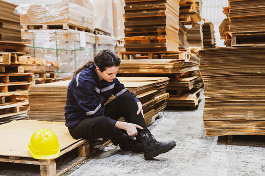 Accident female worker working warehouse factory paper export industry sitting calf pain from cramps massaging legs ankle pain massaging relieve aches and pains from walking working too much.