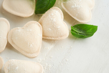 Italian ravioli pasta in heart shape. Tasty raw ravioli with flour and basil on white background. Food cooking ingredients background. Valentines or Mothers Day lunch ideas. Top view with copy space.