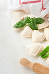 Italian ravioli pasta in heart shape. Tasty raw ravioli with flour and basil on white background. Food cooking ingredients background. Valentines or Mothers Day lunch ideas. Top view with copy space.