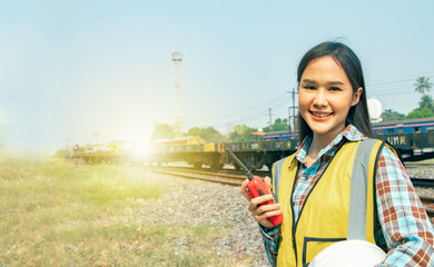 Portrait professional Asian female worker engineer working in outdoor field at diesel locomotive train station, holding walkie talkie and helmet, smiling at camera in elegant pose.