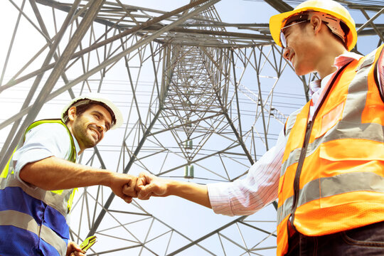 Caucasian male architect and worker asian engineer electrician bumping fists working as a team colleagues believe positive approach to success planning sustainable high voltage electric power project.