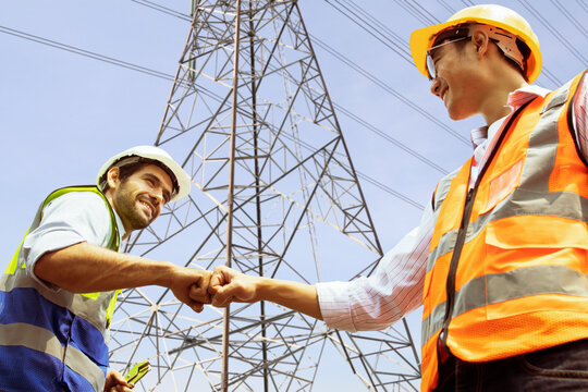 Caucasian male architect and worker asian engineer electrician bumping fists working as a team colleagues believe positive approach to success planning sustainable high voltage electric power project.