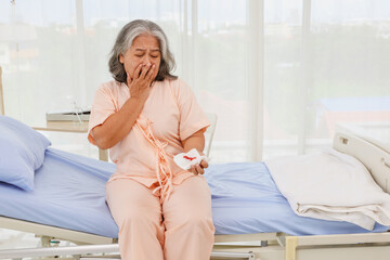 Elderly asian woman stressed, cry worry sitting on a bed hospital emergency room suffering from...