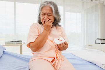 Elderly asian woman stressed, cry worry sitting on a bed hospital emergency room suffering from...
