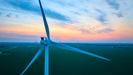 Aerial gorgeous sunset over wind farm and green farmland with close up of wind turbine