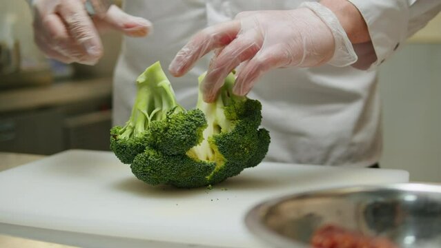 Head chef cutting broccoli with knife on white desk in restaurant cafe kitchen. Close-up of broccoli vegetable slicing 