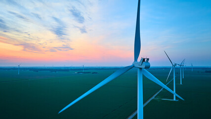 Green farmland with rows of wind turbines on wind farm aerial at gorgeous pink and orange sunset