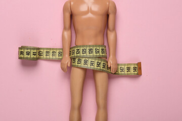 Naked male doll wrapped in measuring tape on a pink background - obrazy, fototapety, plakaty