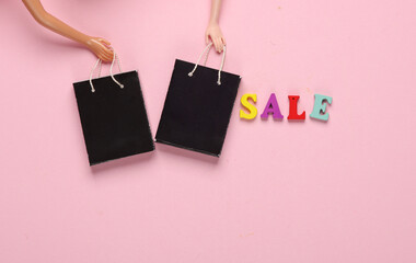 Doll hands holding Miniature shopping bags and word sale on pink background. Black Friday, world shopping day, sale