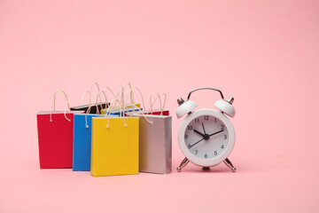 Miniature shopping bags and alarm clock on pink background. Black Friday, world shopping day, sale...