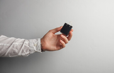 Man's hand in white shirt holds miniature shopping bag on gray background.  Black Friday, world shopping day, sale concept