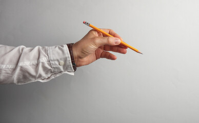 Man's hand in white shirt holds pencil on gray background. Business concept