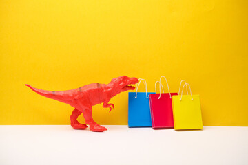 Toy tyrannosaurus with a shopping bag on yellow background. Minimalism shopping concept