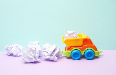 Toy dump truck with crumpled balls of paper on pastel background