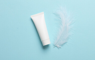 White cream tube with soft feather on a blue background