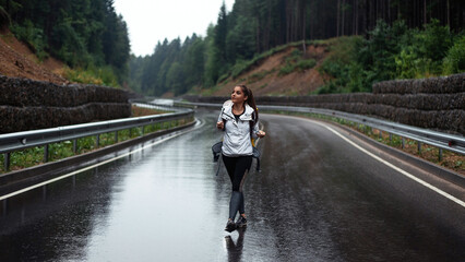 Female tourist with backpack walking during rainy weather at green beautiful mountains