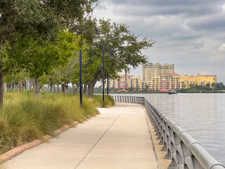 Perspective of municipal riverwalk in Bradenton, Florida, with view of speedboat passing by condominiums along Manatee River, on a cloudy afternoon at the end of September