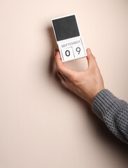 Man's hand in a sweater holds block calendar with the date september 9 on a beige background