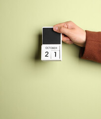 Man's hand in coat holds block calendar with the date october 21 on green background