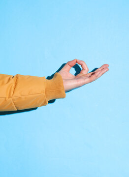 Male hand in a warm winter jacket showing zen cymbol on a blue background