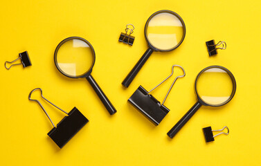 Magnifiers and paper binders on yellow background. Top view
