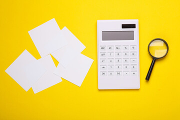 Memo pieces of paper, calculator and magnifying glass on yellow background. Business concept