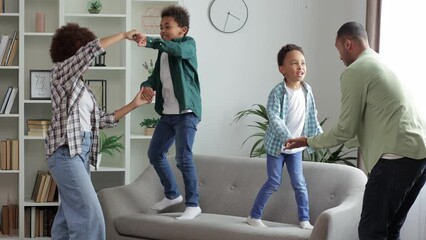 Happy family dancing having fun together with little sons in modern living room. Young dad and mother with adorable cute children enjoying weekend at home.