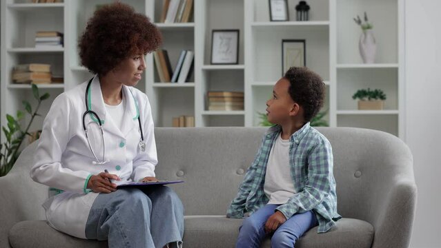 Young african american female doctor pediatrician talking to kid boy patient making notes in clipboard card explaining health care to black school teenager fill form at medical checkup appointment