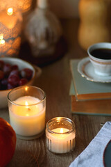 Cup of tea or coffee, plate with desserts, dried oranges, bowl of grapes, scented candles, vintage books, pumpkins and autumn leaves on the table. Autumnal hygge. Selective focus.