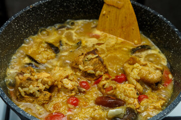 Braised eggplants with meat and rice in Israeli spices in a cast-iron high frying pan with a wooden spatula.