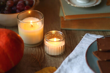 Cup of tea or coffee, plate with desserts, dried oranges, bowl of grapes, scented candles, vintage books, pumpkins and autumn leaves on the table. Autumnal hygge. Selective focus.