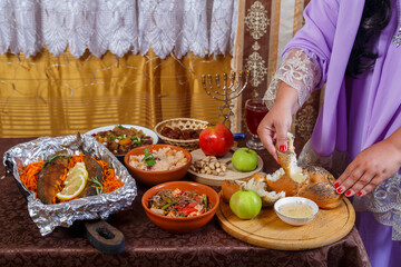 A woman's hand dips a piece of challah in honey at a set table on the Jewish holiday of Rosh Hashanah after prayer.