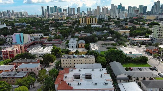 tilt aerial footage of skyscrapers, hotels and apartments in the city skyline, cars on the street, lush green trees and grass, blue sky and powerful clouds in Miami Florida USA
