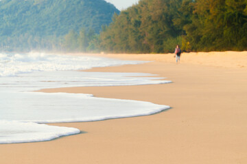 White ocean waves on the beach on a romantic morning and a person walking on the beach