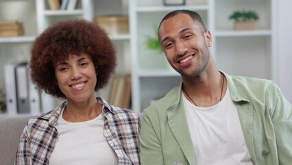 young cheerful marital couple entertaining together at home watching tv while resting on couch. man drinking water